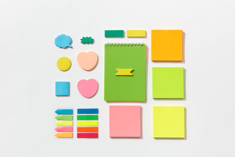 An artistic flat lay of colorful sticky notes and notebook on white background.