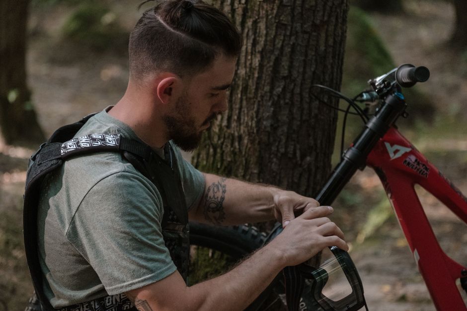 A cyclist adjusts his mountain bike in a forest, readying for an outdoor adventure.