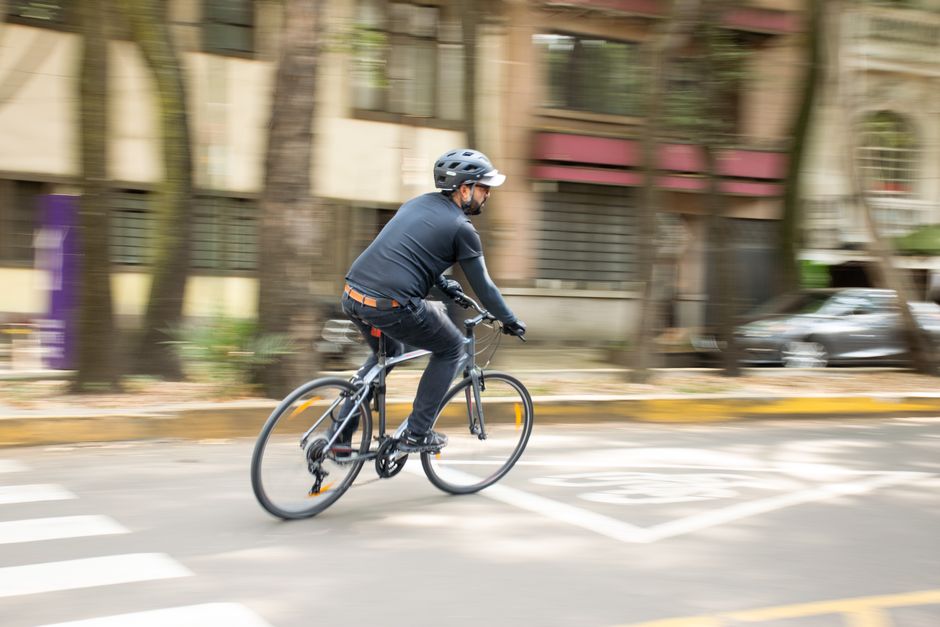 Adult male cycling on city street with helmet, promoting urban mobility.