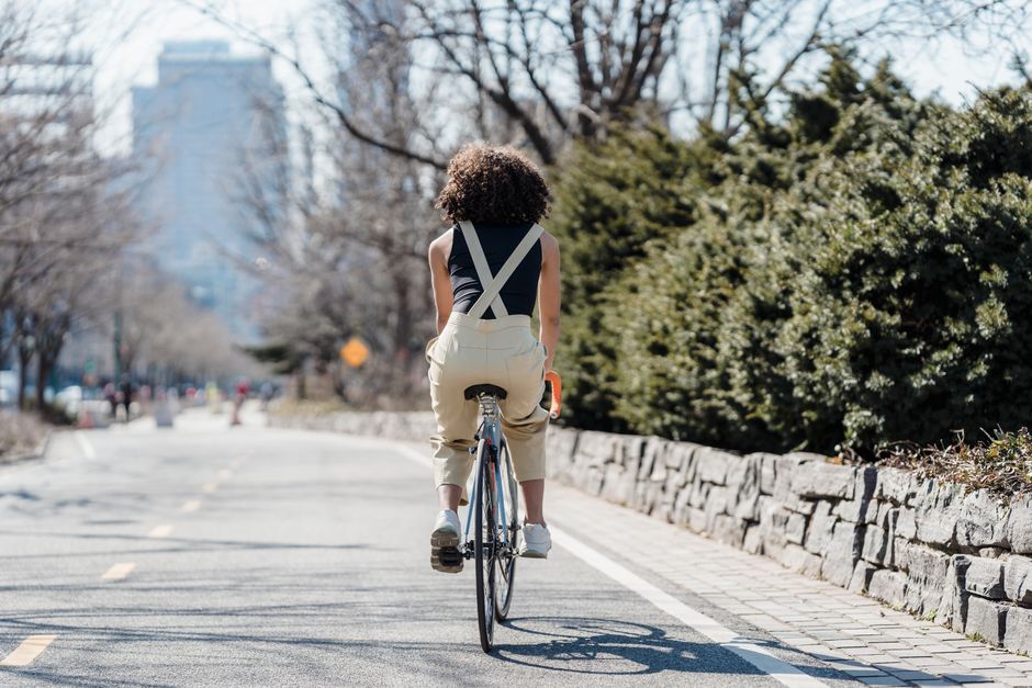 Back view of black anonymous female cyclist riding bicycle on asphalt road in city with gr