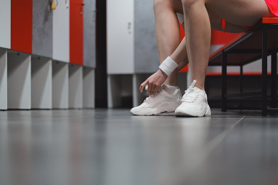 Female athlete tying white sneakers in a gym locker room, ready for exercise.