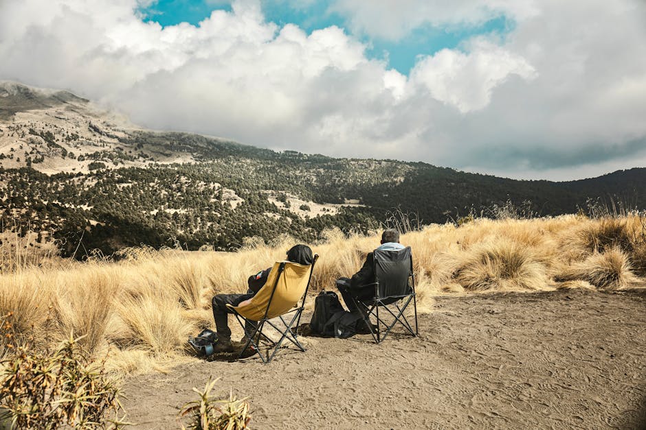 Two hikers sitting in chairs enjoy a scenic mountain view under a cloudy sky.