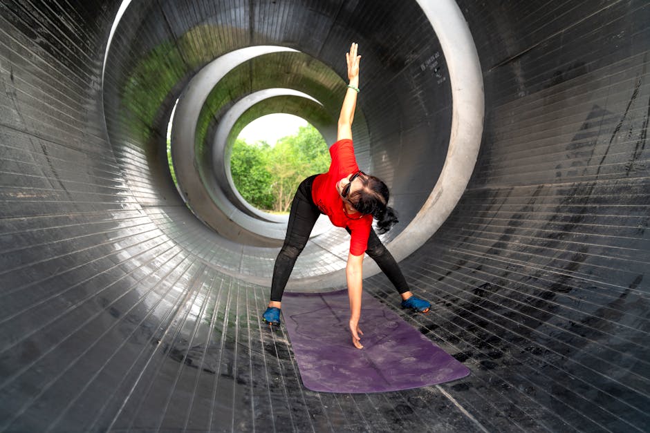A woman engages in yoga stretching inside a circular metal tunnel, emphasizing fitness and wellbeing.