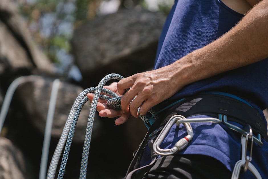 A rock climber tying knots and preparing safety gear for a climb outdoors.