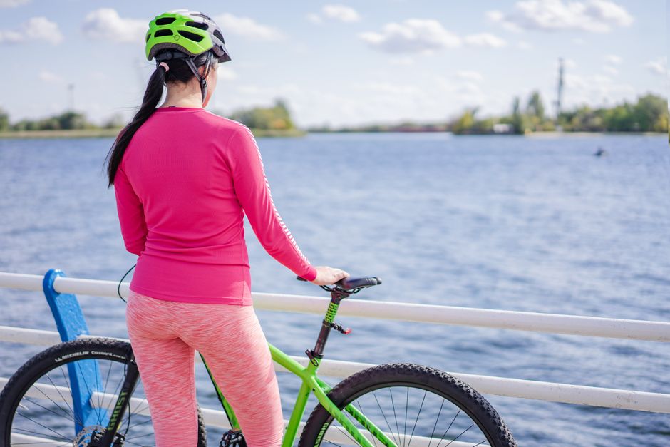 Back view of a woman cyclist by a lake enjoying the outdoors on a sunny day.