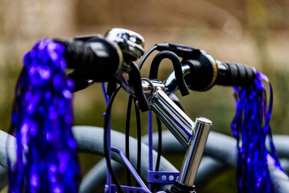 Close-up of a bicycle handlebar with chrome finish and blue tassels outdoors.