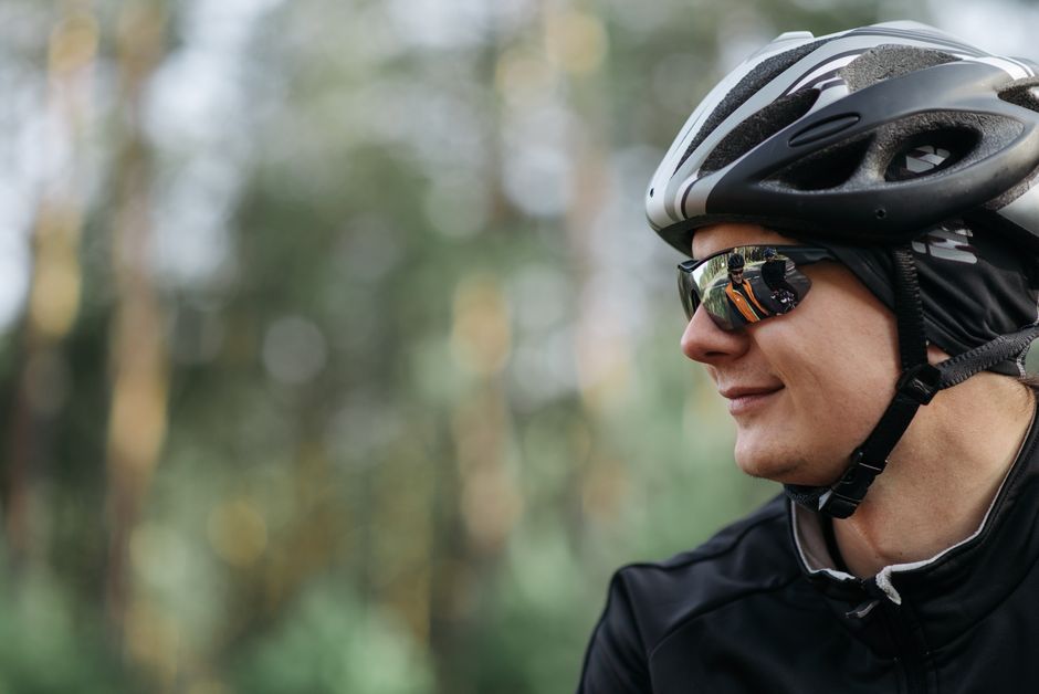 Close-up side profile of a cyclist with helmet and sunglasses in a wooded area