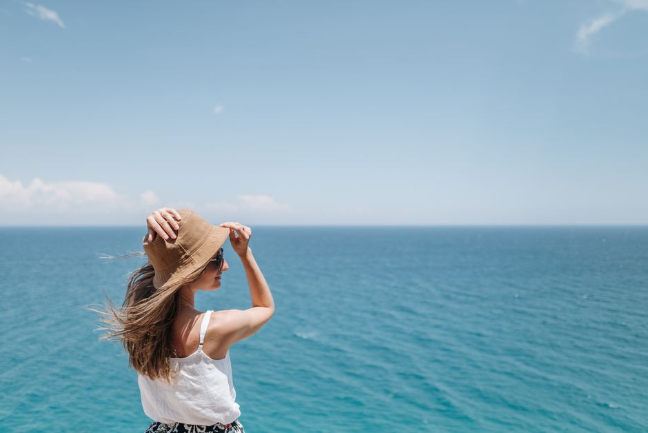 Woman with straw hat and sunglasses enjoying a sunny day by the ocean.