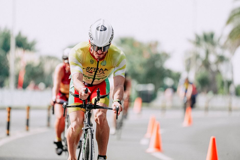 Fit male cyclist in sportswear and protective helmet riding bicycle behind anonymous compe