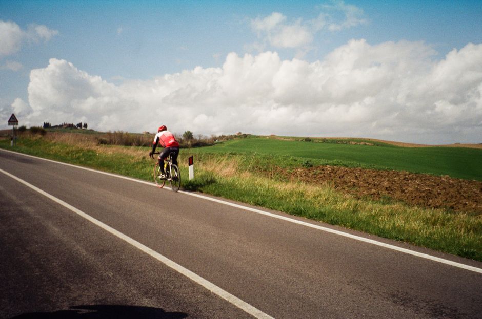 Cyclist in red jersey enjoying a scenic ride on a country road under a cloudy sky.
