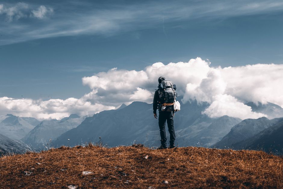 Adventurous hiker standing on a scenic mountain hilltop with a backpack, surrounded by stunning cloudy skies.