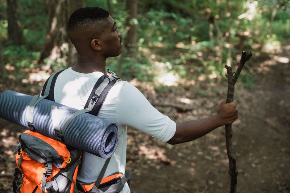Side view of African American hiker standing with wooden stick on path in forest in daytime