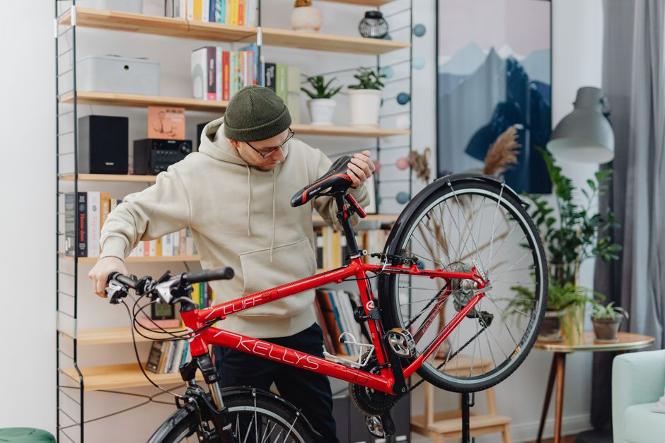 Man lifting a red bicycle indoors near a bookshelf, showing daily handling of a vertical storage setup