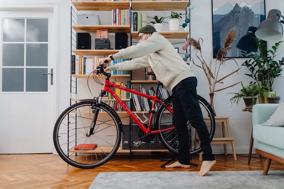 Man positioning a red bicycle onto a freestanding floor stand in a small apartment living room