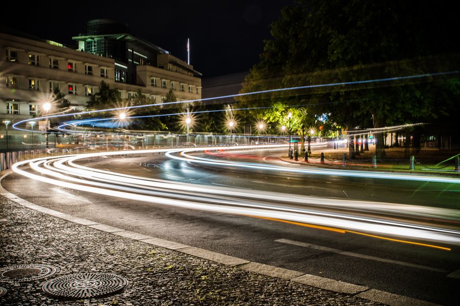 Nighttime city intersection with vibrant light trails and urban buildings.