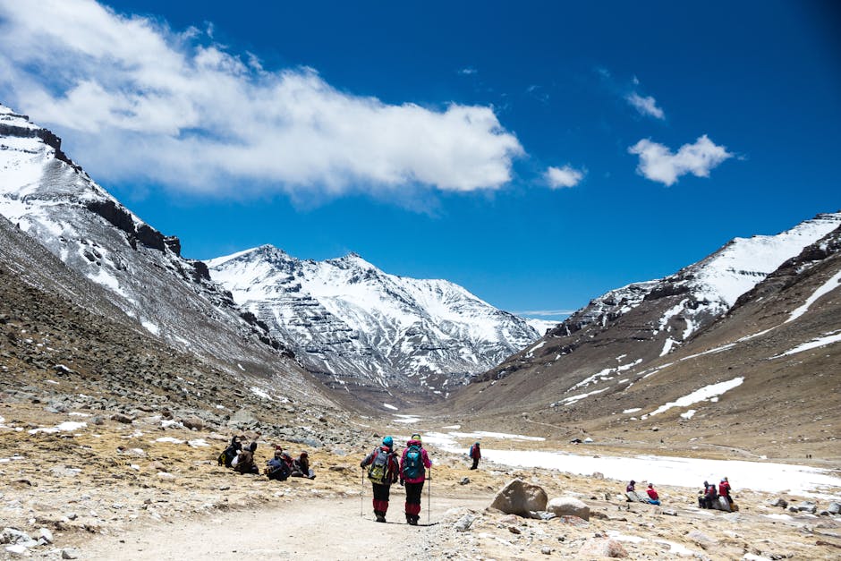 Hikers exploring the stunning snow-capped mountains in Ngari, Tibet under a bright blue sky.