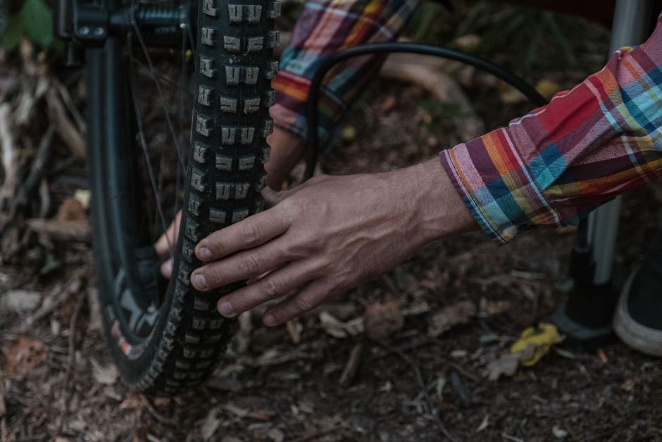Person in plaid shirt inflating a mountain bike tire in a natural setting, highlighting ma