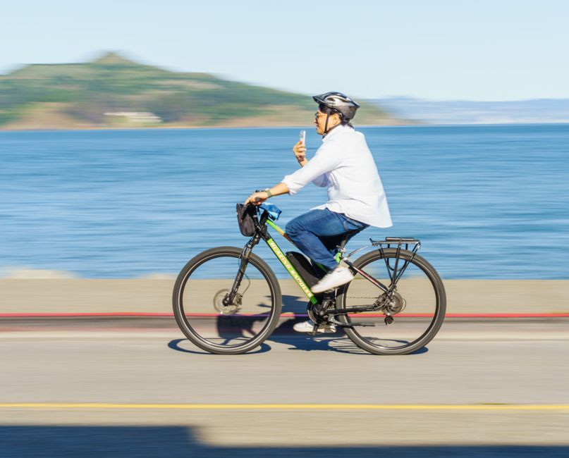 Person riding a bike along a waterfront path, enjoying a sunny day.