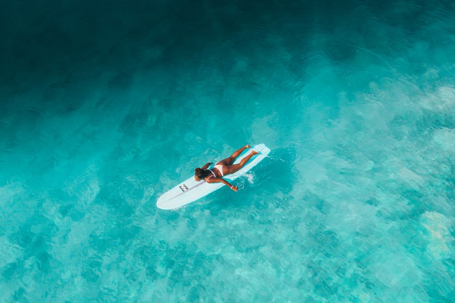 Aerial shot of a girl surfing on turquoise sea waters, embracing island life vibes.