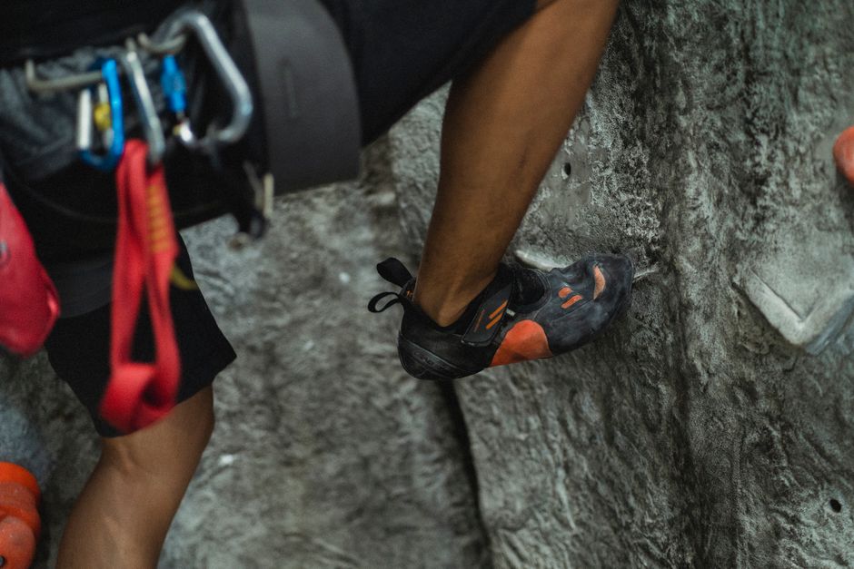 Crop anonymous male alpinist in safety belay with snap hooks clambering wall in bouldering center