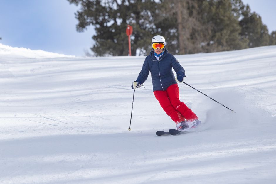 A skier in vibrant winter gear descends a snowy slope on a sunny day.
