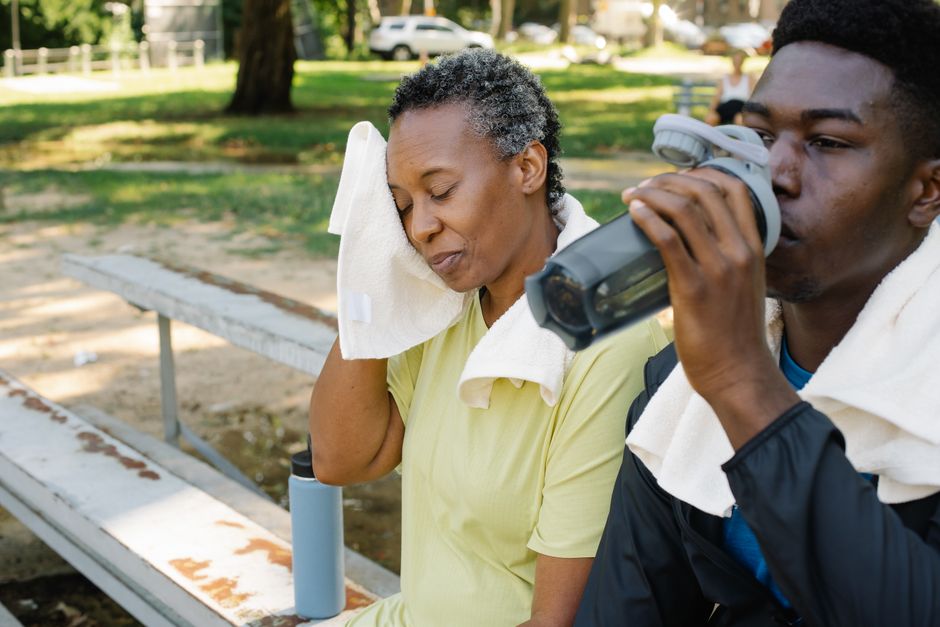 A mother and son refresh themselves at the park with towels and water bottles.