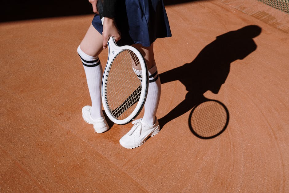 Tennis player in skirt and white sneakers holding racket under sunlight on clay court