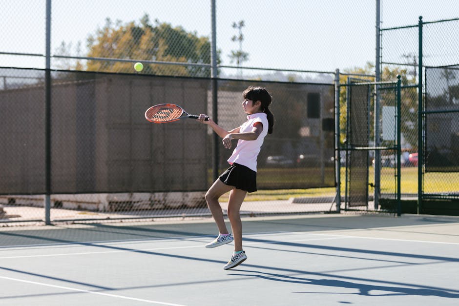 Young girl on tennis court practicing her swing during a lively outdoor match.