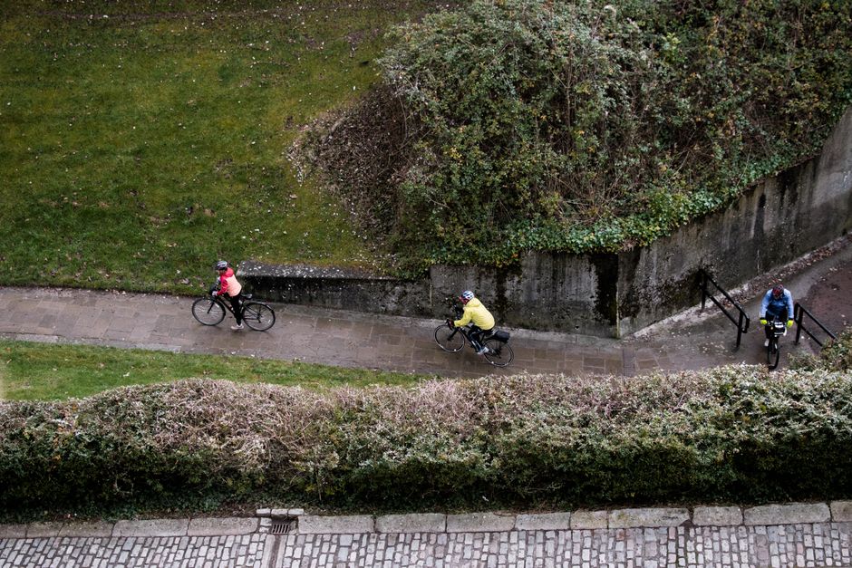 Three cyclists ride along a scenic pathway, surrounded by lush greenery and bushes. Captur