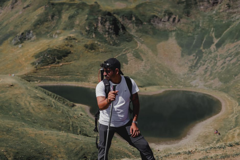A man with a backpack hikes near a serene mountain lake during a sunny summer day.