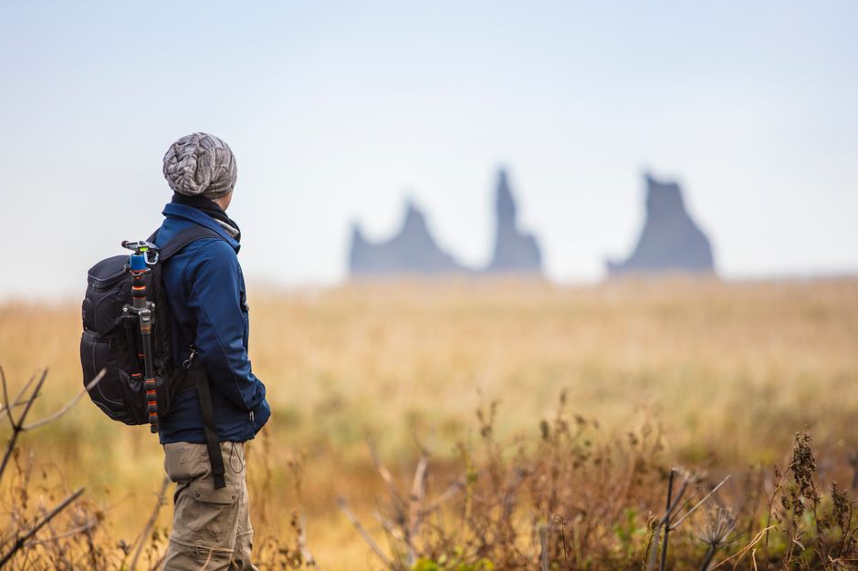 A lone backpacker gazes at distant rock formations in an open grassland, embodying adventure.