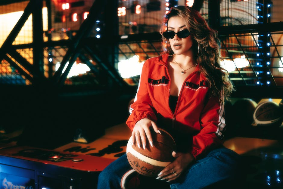 Trendy woman in red jacket holding basketball in a vibrant arcade.