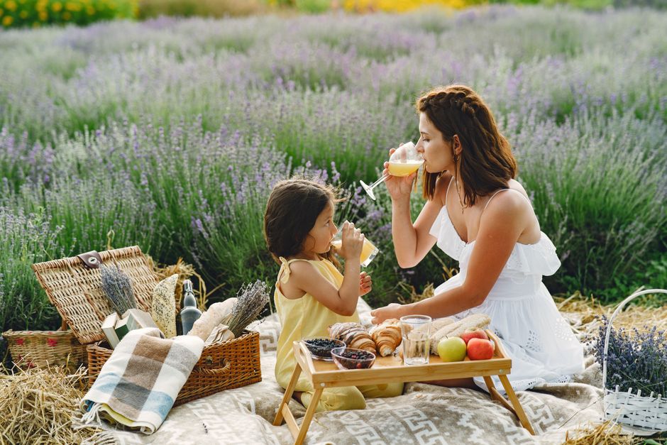Mother and daughter sharing a peaceful summer picnic in a lavender field with fresh fruits and juice.