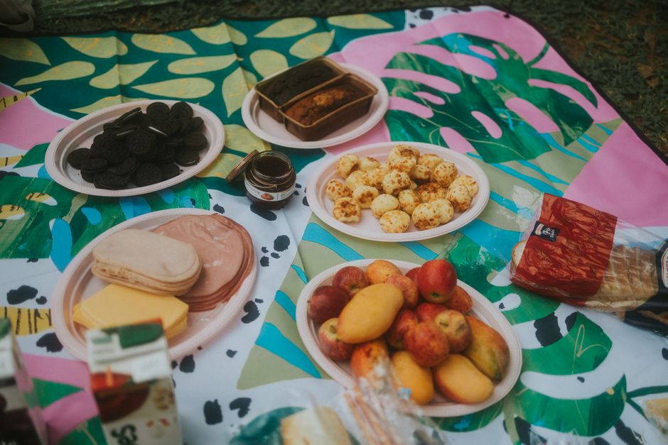 Vibrant picnic layout with fruits, snacks, and patterned blanket outdoors.
