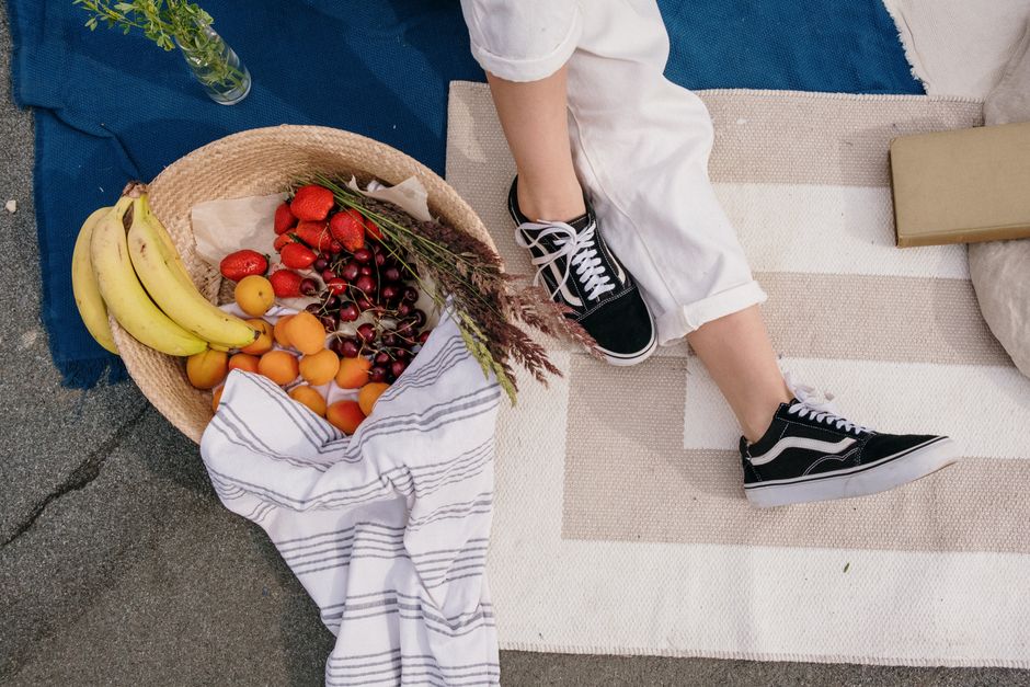 Relaxing outdoor picnic with fresh fruits, sneakers, and a cozy setup under the sun.